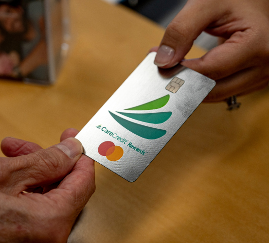 Two hands holding a CareCredit card with a green leaf logo and Mastercard symbol.