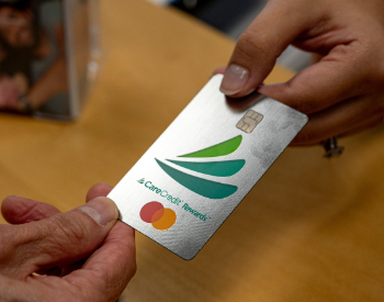 Two hands holding a CareCredit card with a green leaf logo and Mastercard symbol.