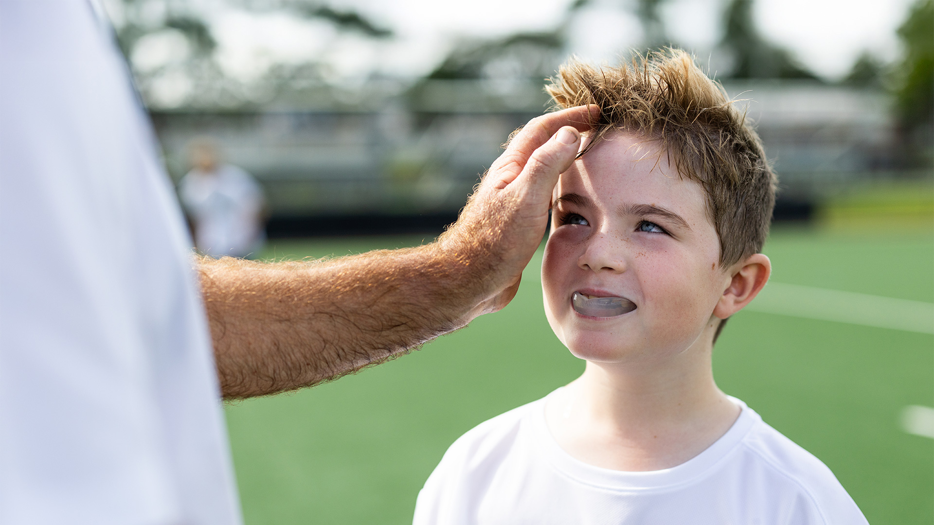 Boy on a sports field wearing a mouthguard while an adult checks his face